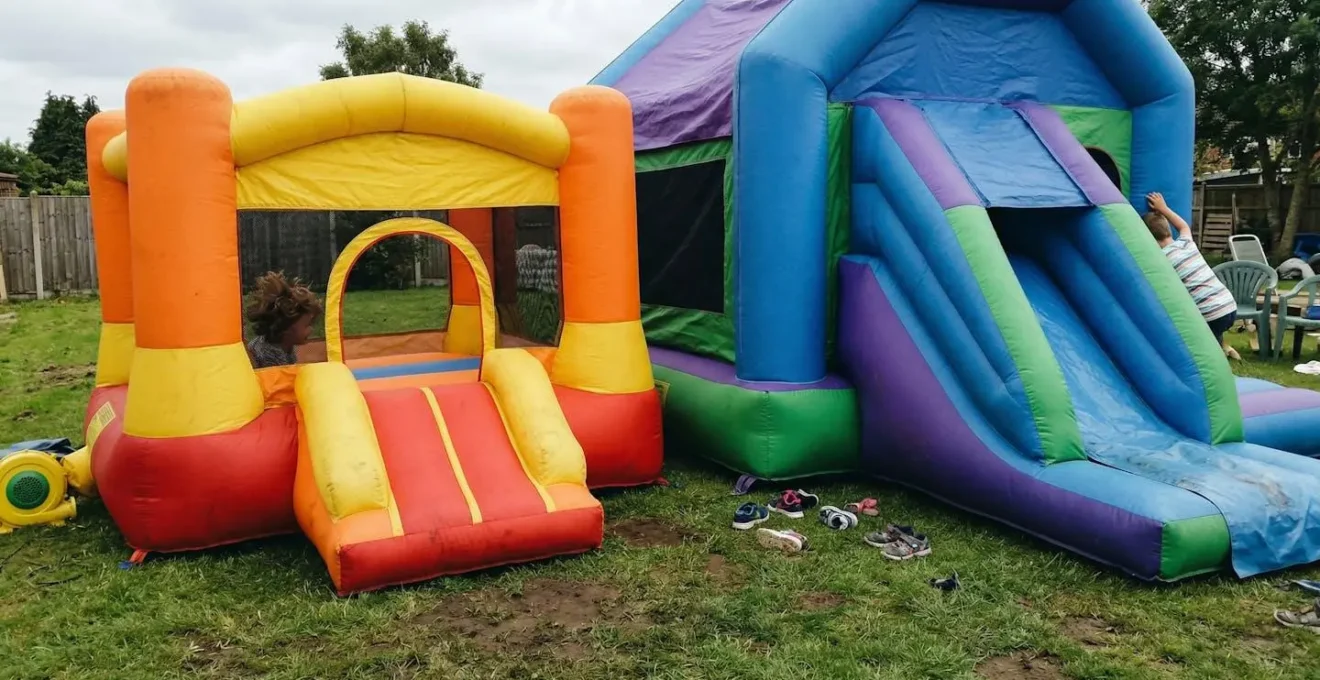 Deux structures gonflables installées côte à côte sur une pelouse, une petite et une grande avec toboggan